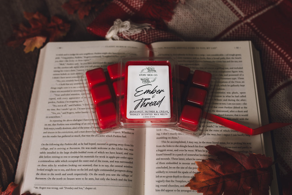 Red wax melts with a labeled container on an open book, surrounded by autumn leaves.