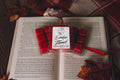 Red wax melts with a labeled container on an open book, surrounded by autumn leaves.