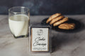 Packaged cookie-scented wax melt with a glass of milk and cookies on a marble surface