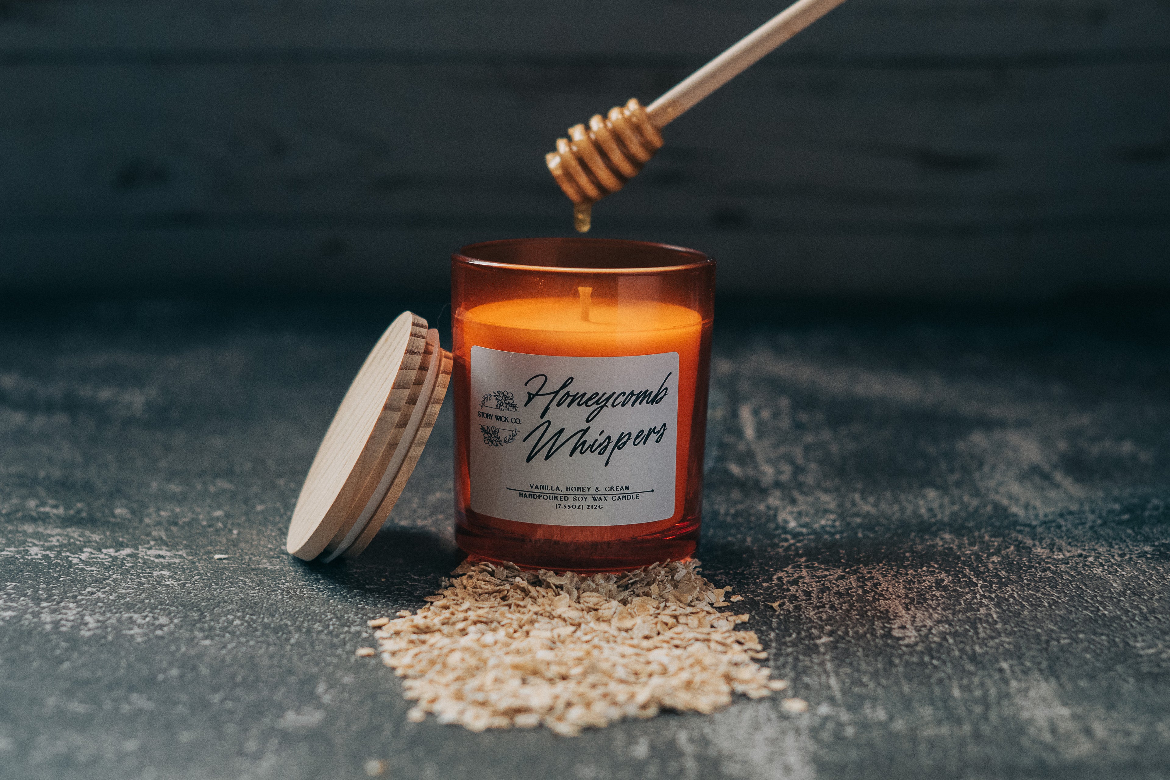 Honeycomb Whispers candle with a honey dipper on a dark surface.