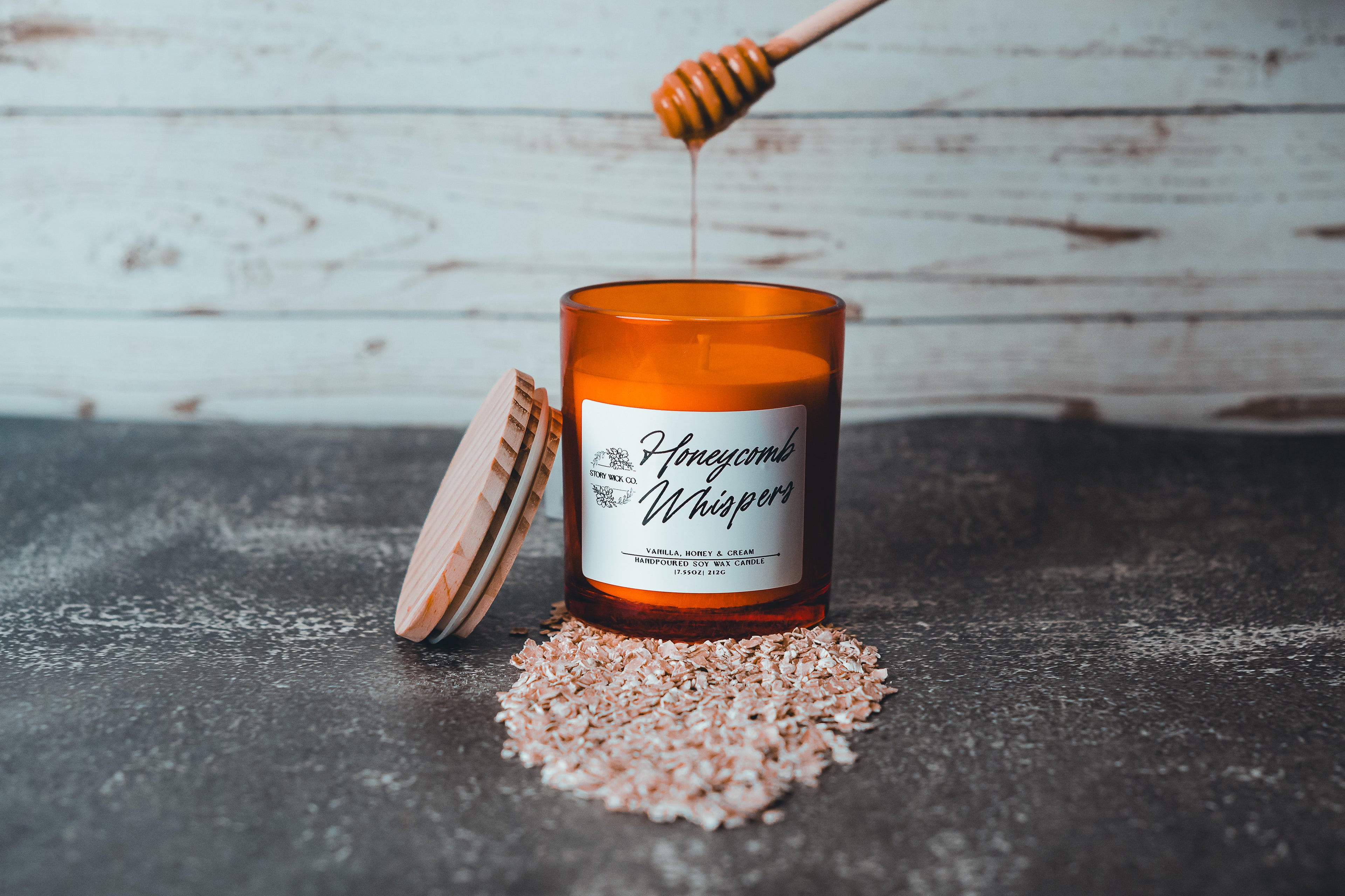 Orange candle labeled 'Honeycomb Whispers' with a honey dipper and honeycomb on a dark surface.