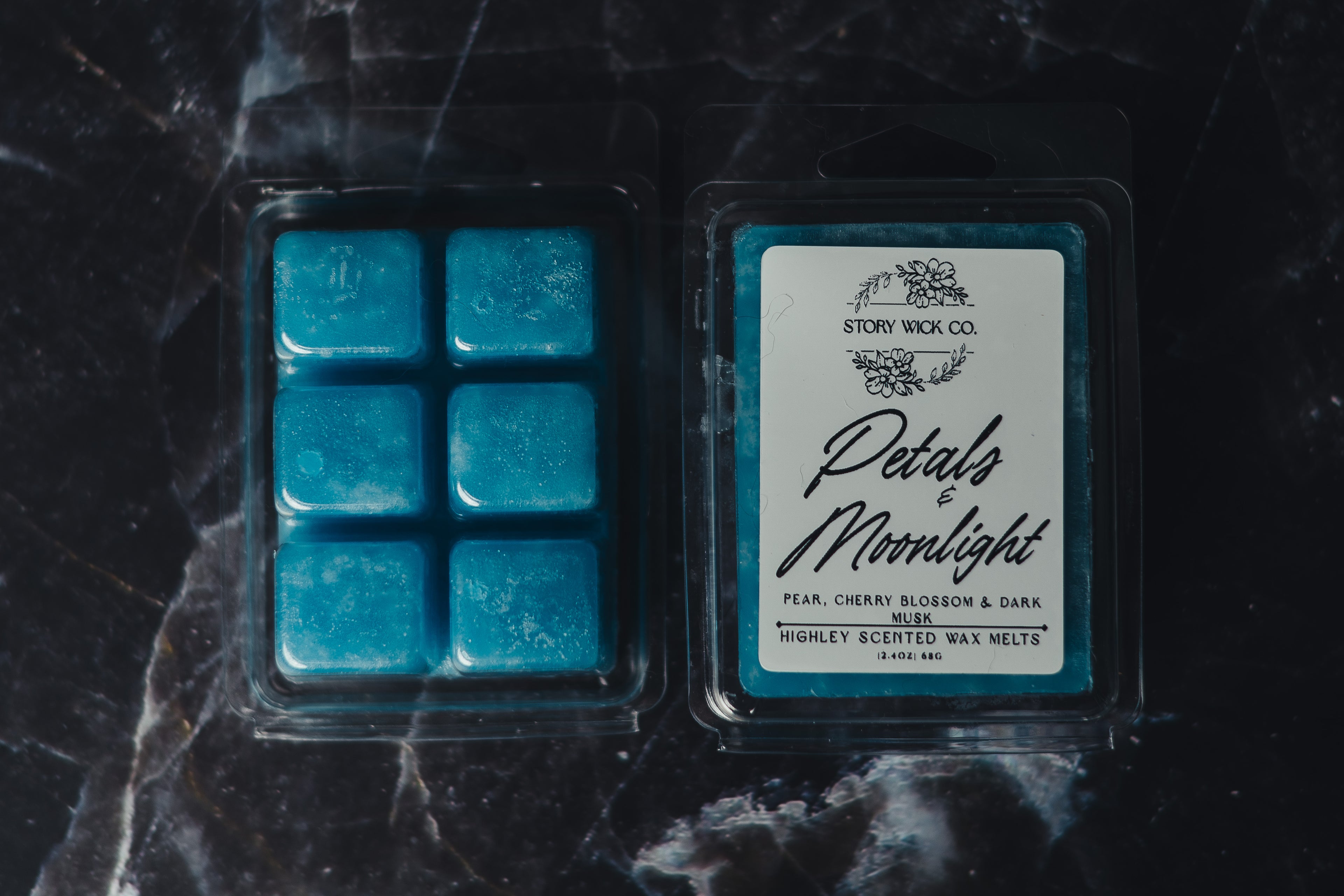 Blue wax melts in a packaging with a label on a dark marble surface.