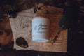 Candle labeled 'Redwood Romance' on a surface with vintage-style text and a feather