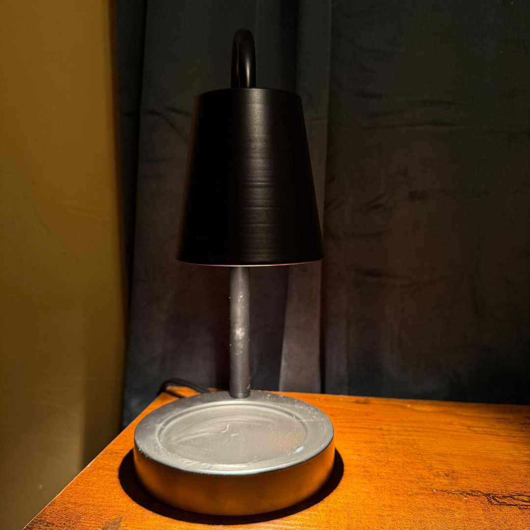 A modern table lamp with a matte black tapered shade and a brushed silver metal base, shown lit on a wooden surface against a dark backdrop.