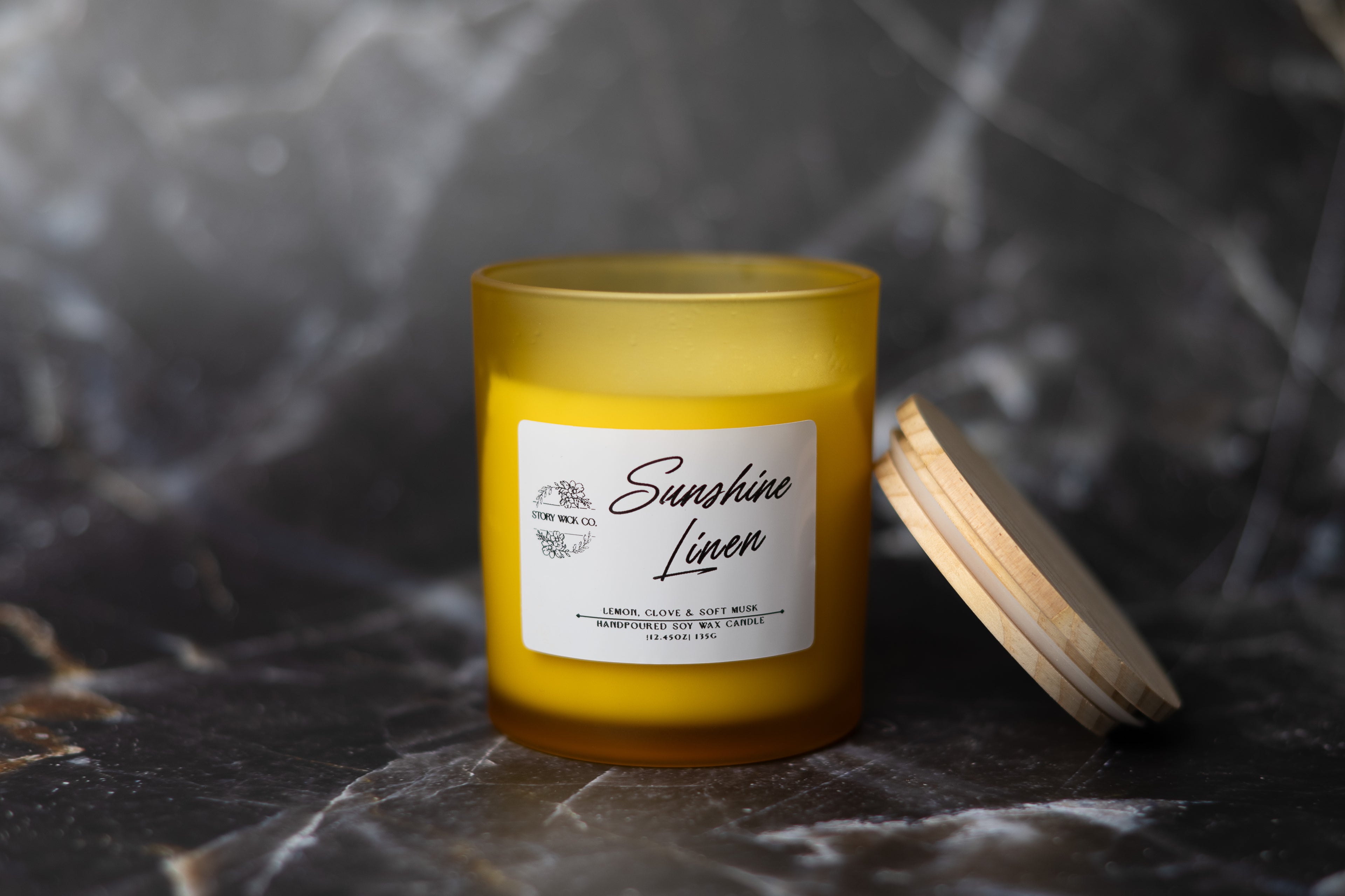 Candle labeled 'Sunshine Linen' on a dark marble surface.