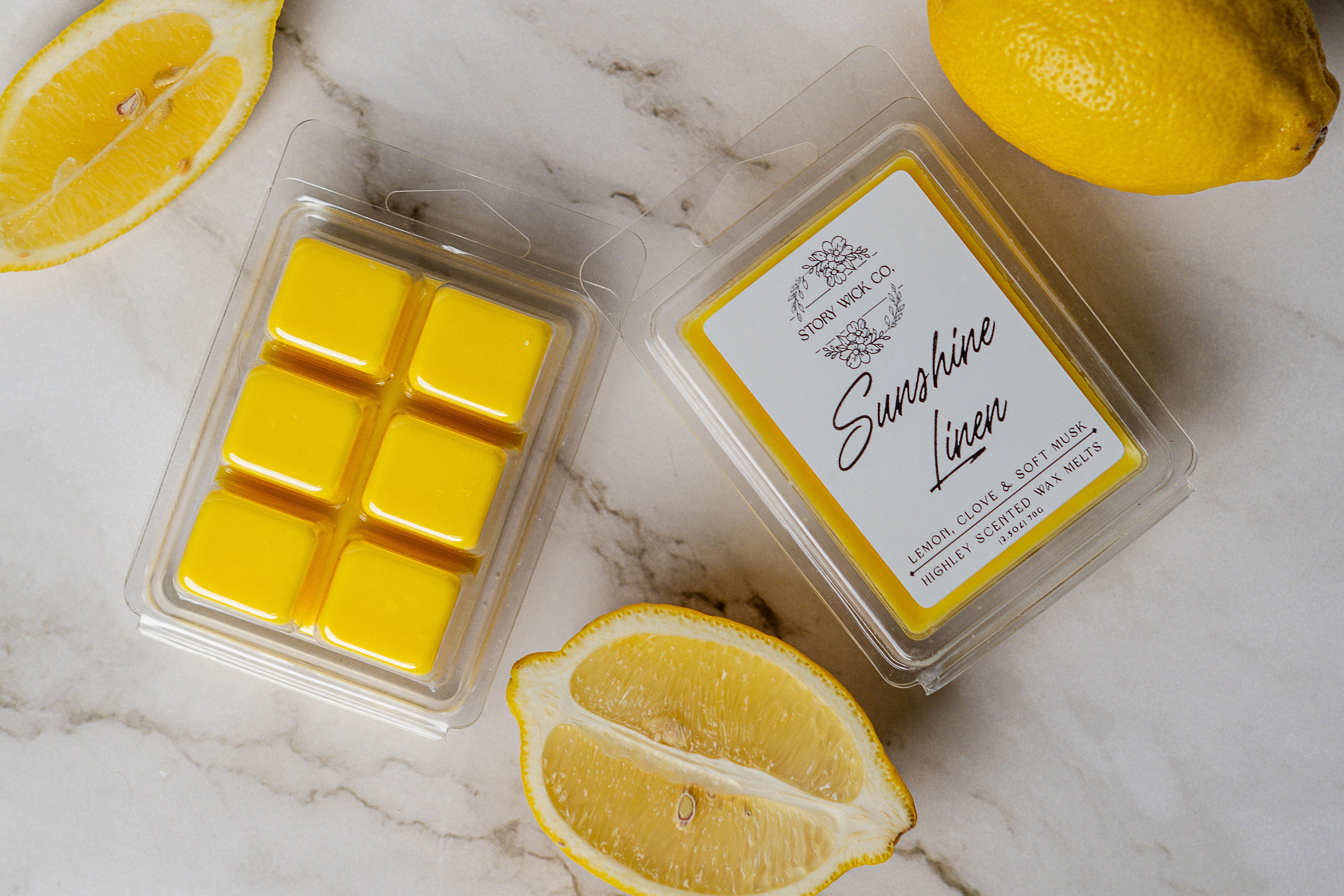 Yellow wax melts in a clear container with a label, surrounded by lemons on a marble surface.